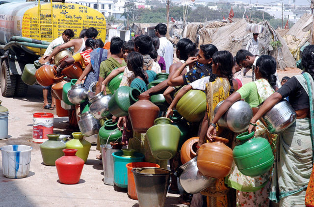 People stand in line with water containers at a mobile drinking water station