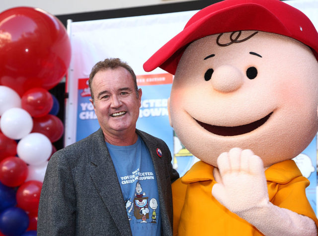 Peter Robbins in a blue t-shirt with a jacket over it standing beside Charlie Brown.