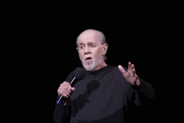 Headshot of George Carlin holding a microphone speaking