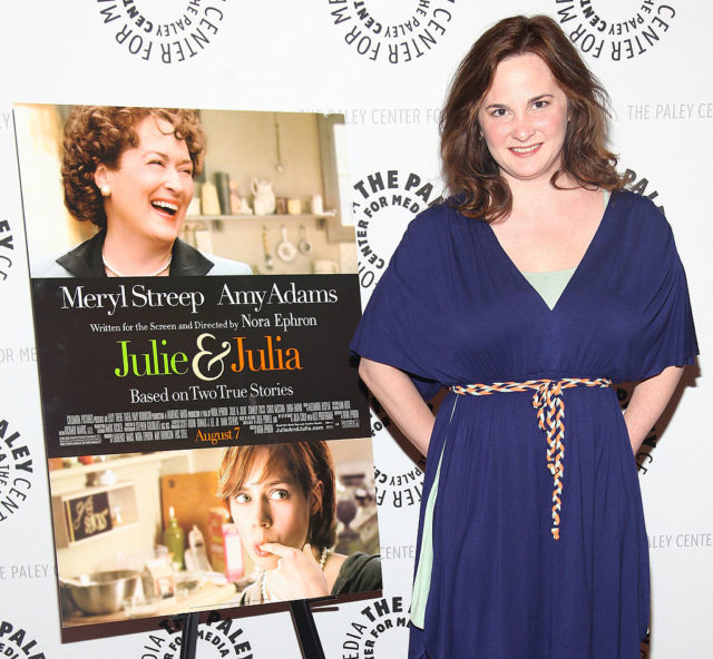 Julie Powell in a blue dress standing beside a 'Julie & Julia' movie poster.