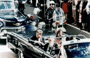 President Kennedy in an open top car beside his wife.