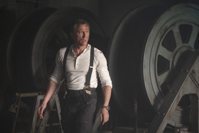 Daniel Craig as James Bond in a white shirt, suspenders, and dark pants.