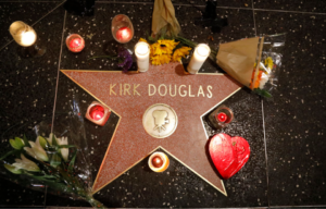 Looking down at Kirk Douglas' Hollywood Walk of Fame star surrounded by candles and flowers.