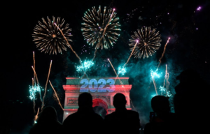 Silhouettes of people watching fireworks with "2023" projected on the Arc de Triomphe.
