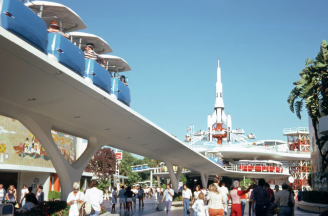 A view from the ground of Disney's PeopleMover, people walking underneath and another ride in the background.