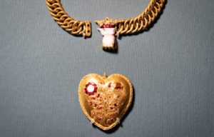 Heart shaped gold pendant with red gems inlaid, and a gold chain.
