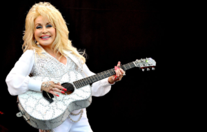 Dolly Parton on stage in a white jumpsuit with a white guitar.