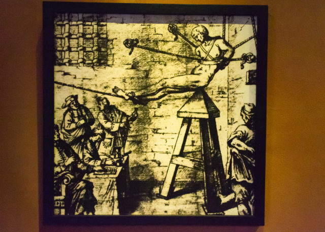 An illustration of a victim placed on a Judas Cradle as torturers watch