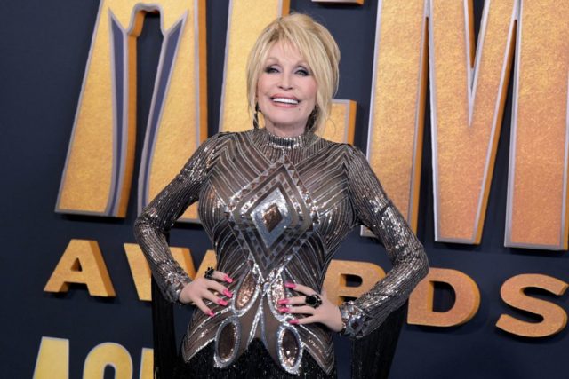 Dolly Parton in a grey and black sparkling dress and her hands on her hips.