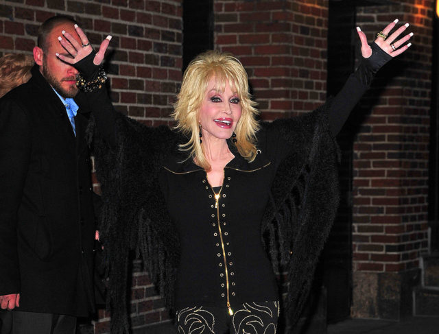 Dolly Parton in all black with her arms in the air, with black fingerless gloves.