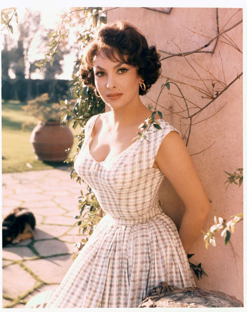 Gina Lollobrigida in a plaid dress posing in front of a wall.