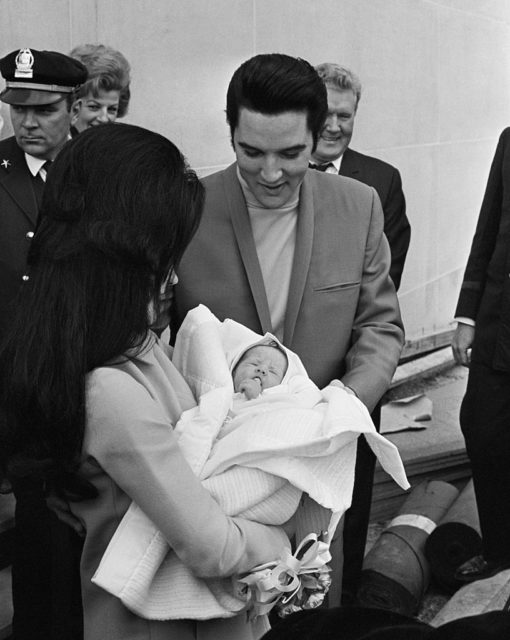 Priscilla Presley holds newborn Lisa Marie in her arms while Elvis looks down at her smiling.