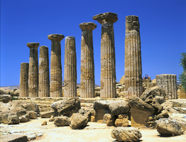 Concrete Roman pillars in a ruinous area, a bright blue sky above