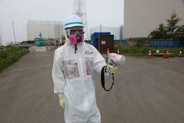 A man in a protective suit holds a Geiger counter device