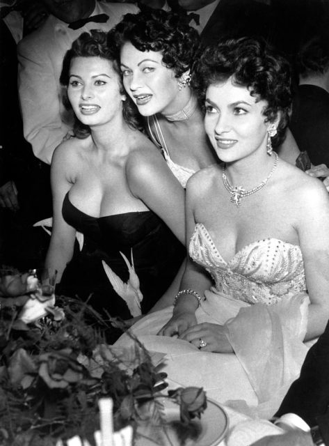 Sophia Loren, Yvonne de Carlo, and Gina Lollobrigida pose in elegant dresses while seated.