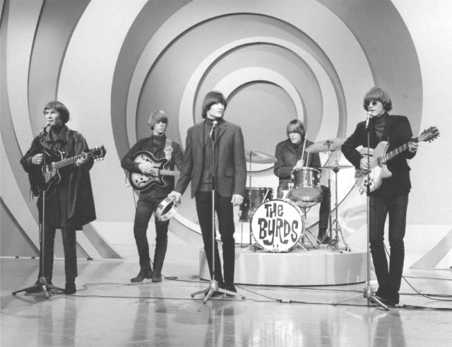 The Byrds playing instruments on stage with a circular background.