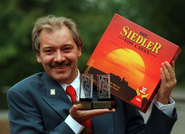 Klaus Teuber holding Catan and two trophies