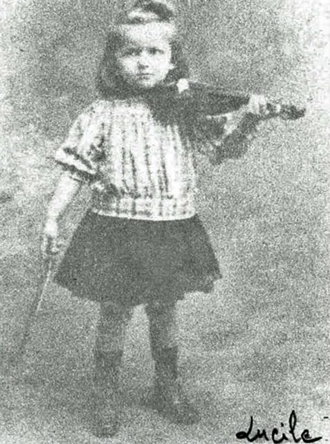 Lucile Randon as a young girl in a skirt and top holding a violin.