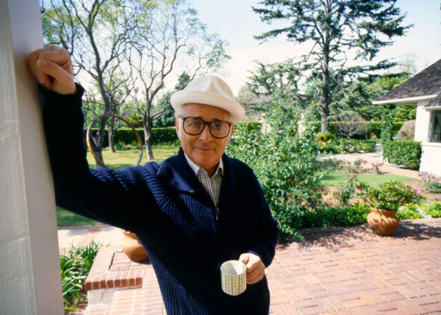 Norman Lear leaning against a doorway while holding a cup of coffee
