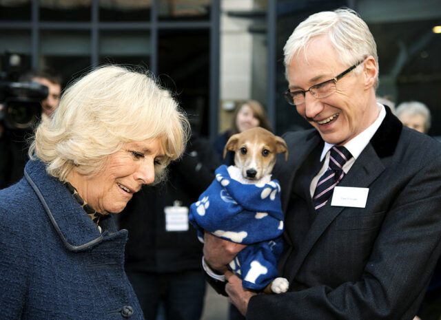 Camilla, Duchess of Cornwall standing with Paul O'Grady, who's holding a dog