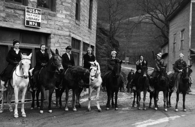 A lineup of women outside of a brick building sitting on horseback. 