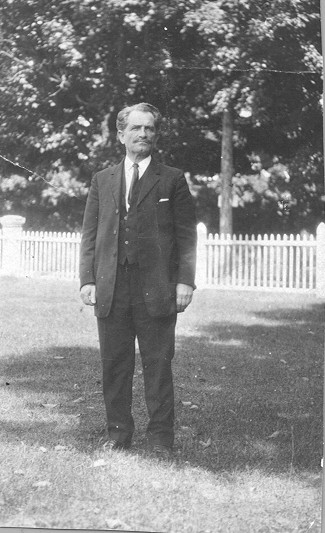 Boris Sidis in a full suit standing outside in front of a white fence.