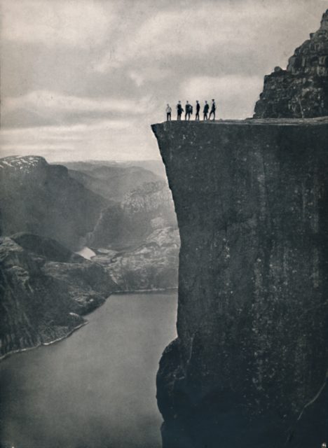 A group of people stand close to the edge of a cliff's edge.