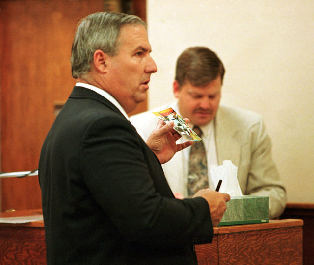 Jim Yontz stands in court holding a photograph.