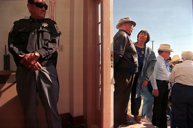 Two sheriffs stand at a door, keeping a line of people in order. 