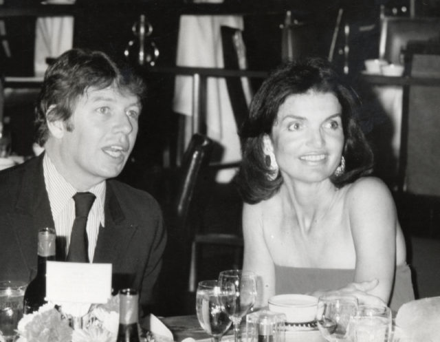 Jackie Kennedy sitting with Peter Hamill at a dining table. 