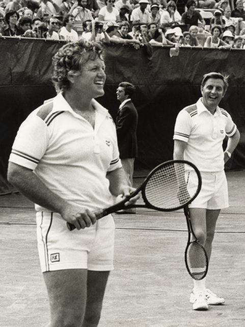 Two men standing on a tennis court holding tennis rackets.