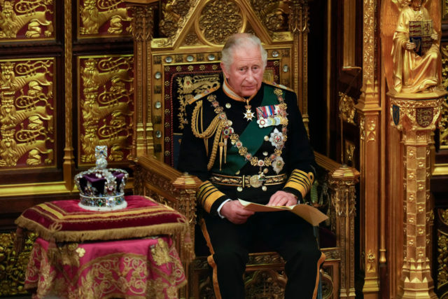 Charles III sitting on a throne next to the Imperial State Crown