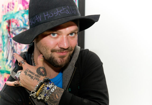 Headshot of Bam Margera showing his forehand wearing a hat and several rings and bracelets