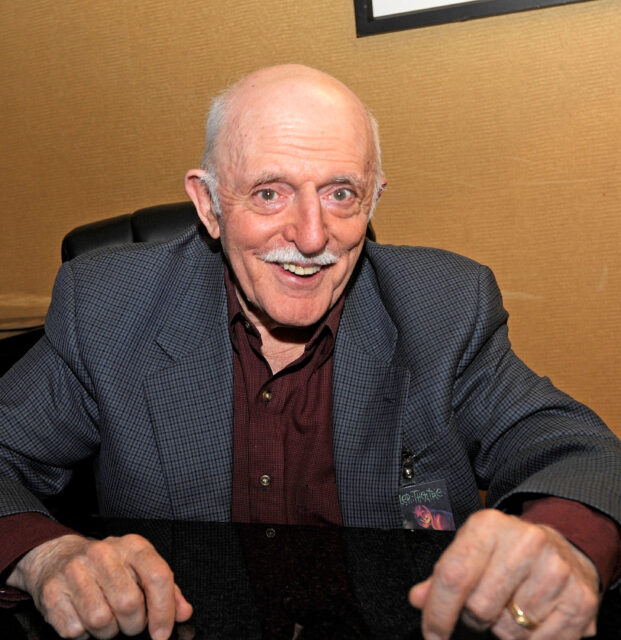 John Astin poses at a desk