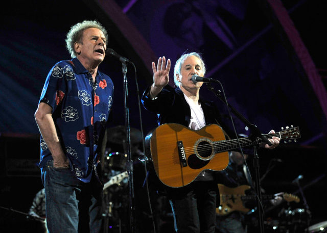 Art Garfunkel and Paul Simon singing on stage standing beside each other. 