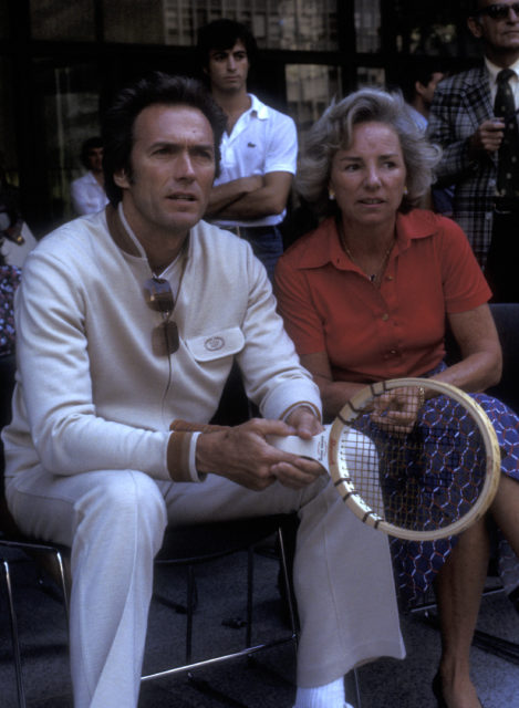 Clint Eastwood sitting beside Ethel Kennedy, holding a tennis racket.