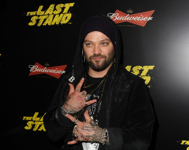 Bam Margera holding up rocker signs wearing a hood.