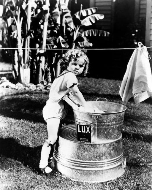 Shirley Temple washing laundry in a bin outside under a clothesline.
