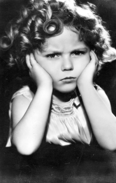 Headshot of Shirley Temple frowning with her hands to her cheeks.