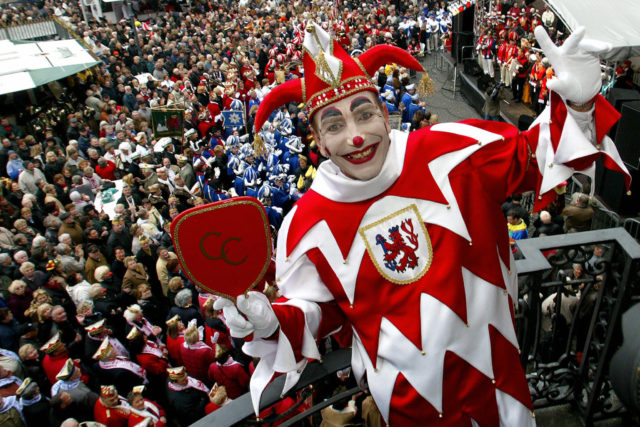 A jester smiles at the camera above a crowd of people