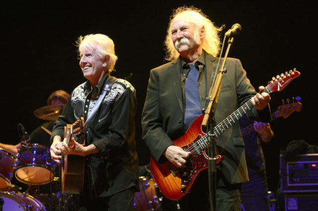 Graham Nash and David Crosby playing guitars on stage and smiling.