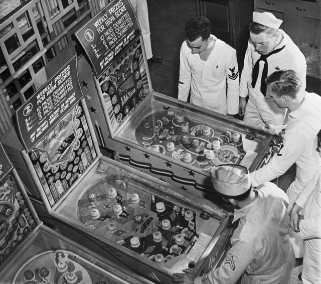 Group of American sailors in uniform playing pinball.