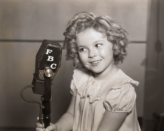 Shirley Temple holds a microphone