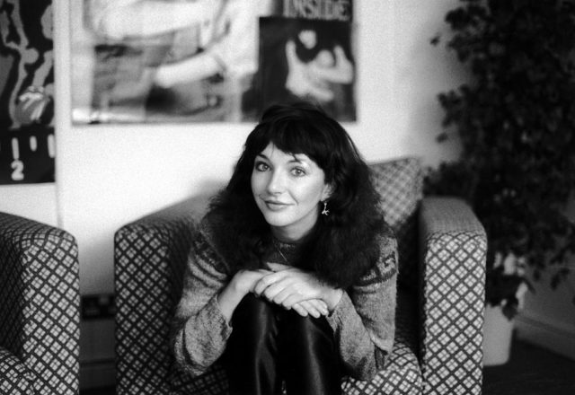 Kate Bush seated in a chair with her arms around her knees.