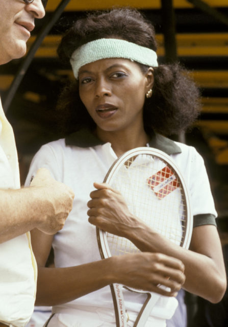 Diana Ross in a headband holding a tennis racket.