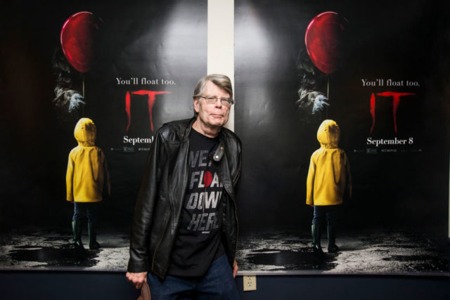 Stephen King standing in front of two movie posters for It. 