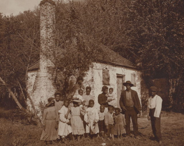A family of former slaves in front of a slave quarters building