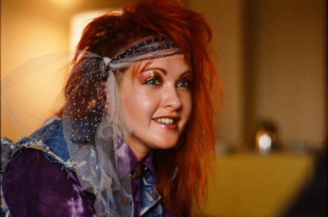 Cyndi Lauper wearing a jean vest, with tulle wrapped around her red hair.