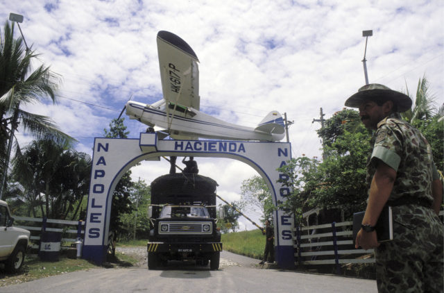 An archway over a driveway with a small plane on top. A truck driving under it with a soldier in the foreground.