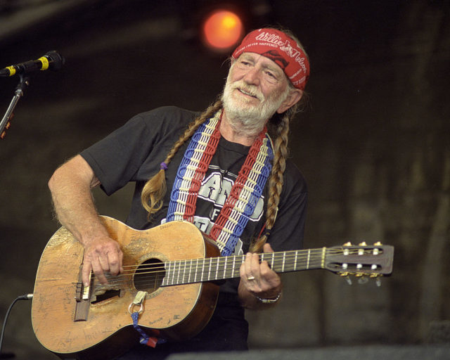 Willie Nelson playing a guitar with his har in two braids.